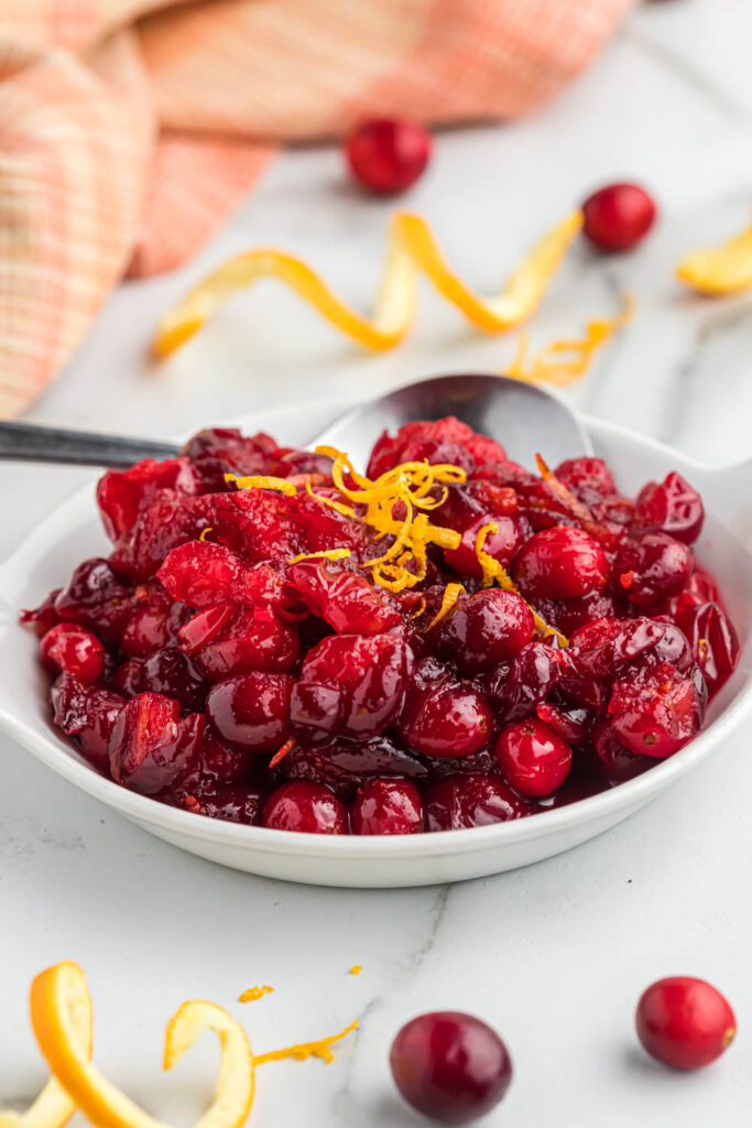 orange cranberry sauce in white bowl with spoon.